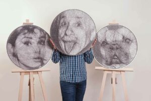 Na zdjęciu widać trzy portrety wykonane techniką string art: dwie z nich są zaprezentowane na sztalugach, a jedną trzyma autor, zasłaniając sobie twarz. Portrety przedstawiają kolejno: Audrey Hepburn, Alberta Einsteina i pyszczek buldoga francuskiego.
