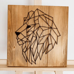 Obraz String Art przedstawiający zwierzęcego patronusa – lwa. Do wyplatania użyto ciemnych nici i jasnych desek.